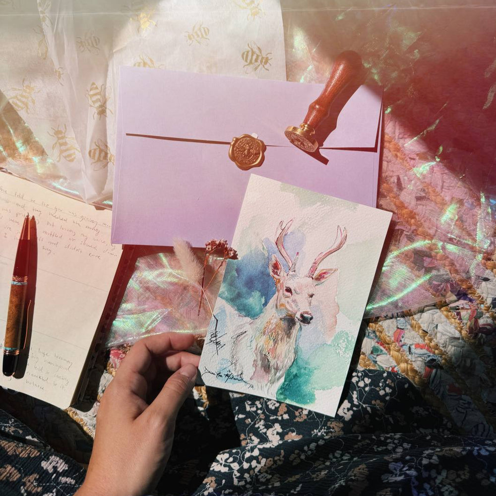 A small original deer watercolor beside a wax-sealed envelope and journal.